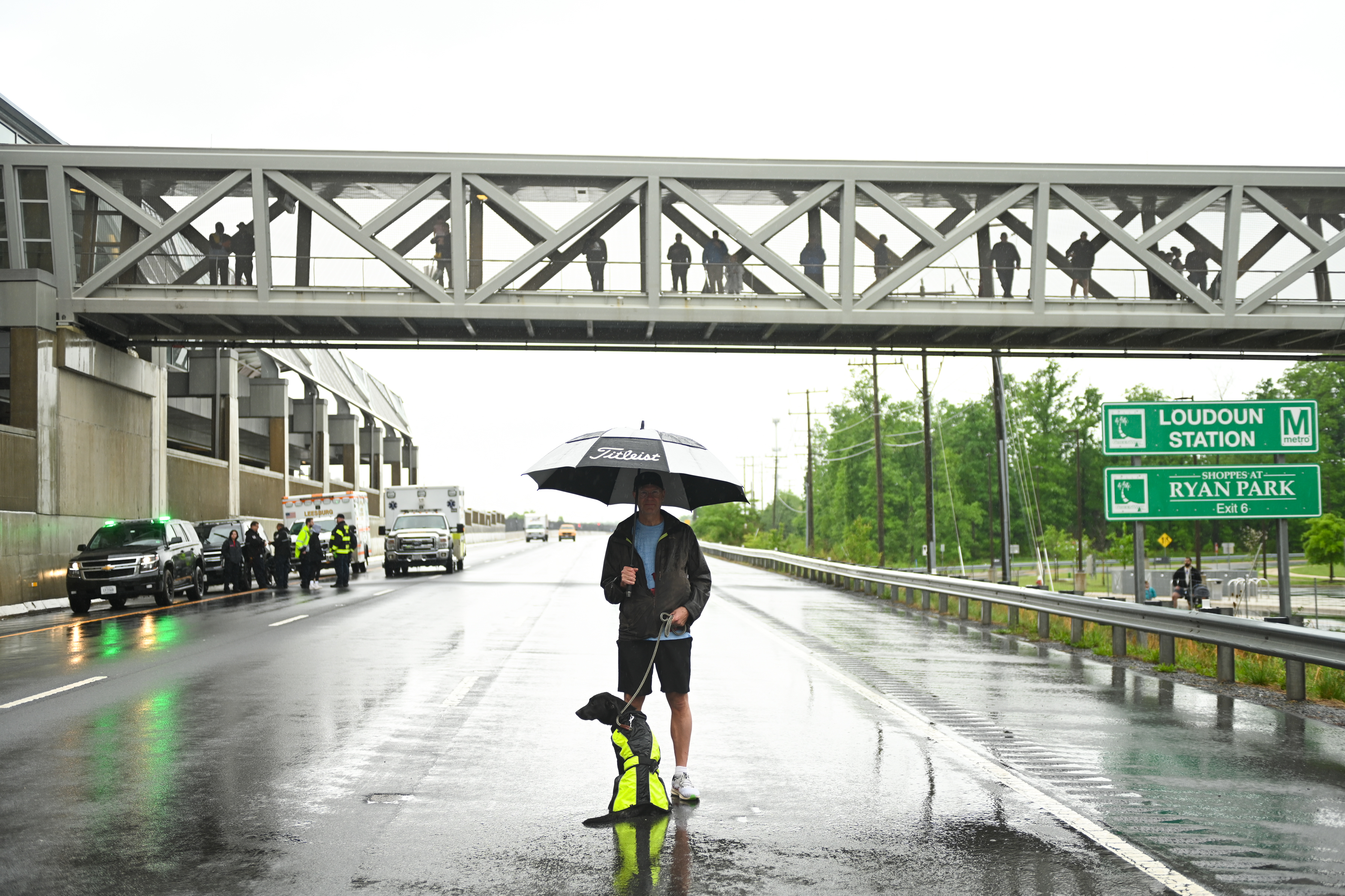 A man and his dog wait in the pouring rain just past the finish line at the 2025 Run the Greenway 5K/10K. This is how it feels when you can't race and you love racing energy.
